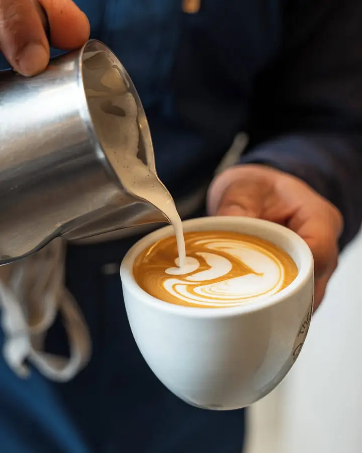 Barista a desenhar latte art numa chávena branca