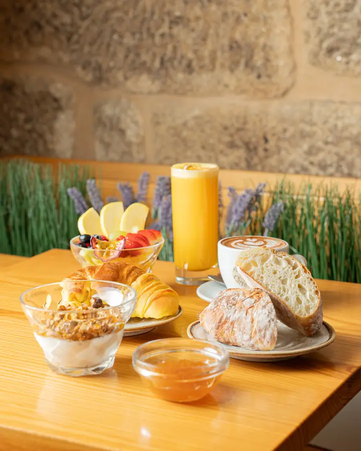Mesa de pequeno-almoço com iogurte e granola, fruta, pão, croissant e sumo de laranja