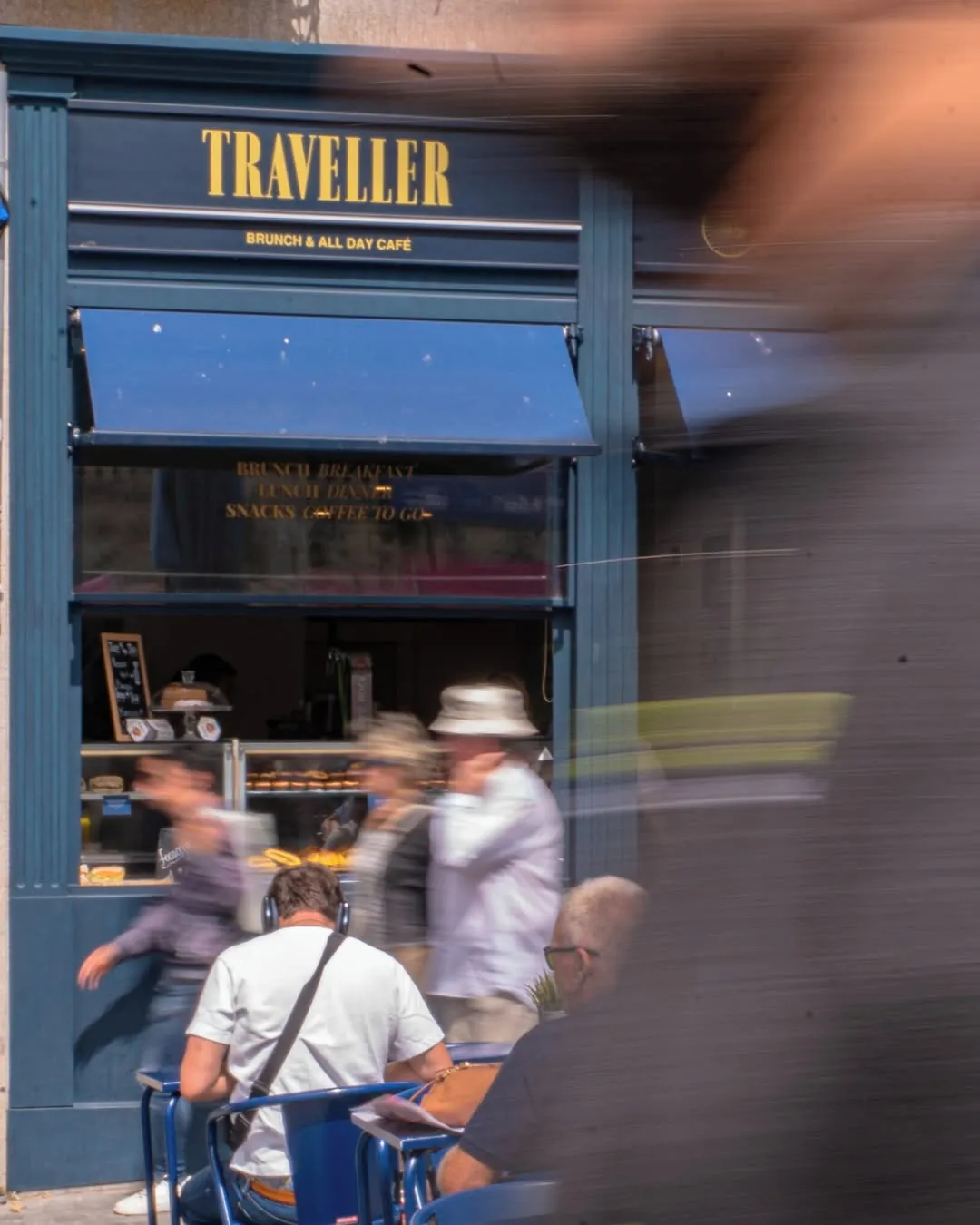 Fachada azul do Traveller, na Praça Almeida Garrett, com pessoas a passar na rua
