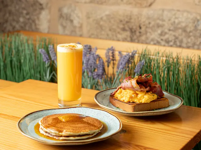 Mesa de brunch com panquecas, ovos mexidos com bacon e sumo de laranja