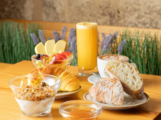 Mesa de pequeno-almoço com iogurte e granola, fruta, pão, croissant e sumo de laranja